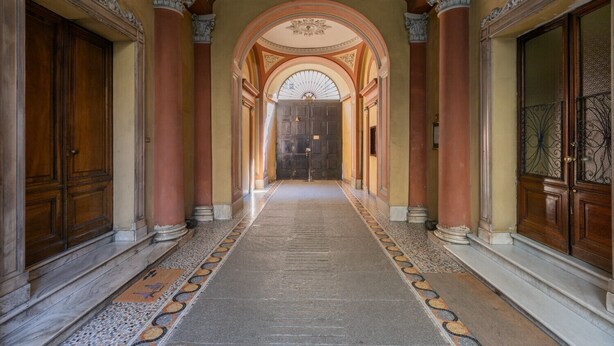 A grand hallway with ornate columns, a patterned carpet, and a large arched doorway at the end. - L Angolo del Libro by Wonderful Italy (Turin)