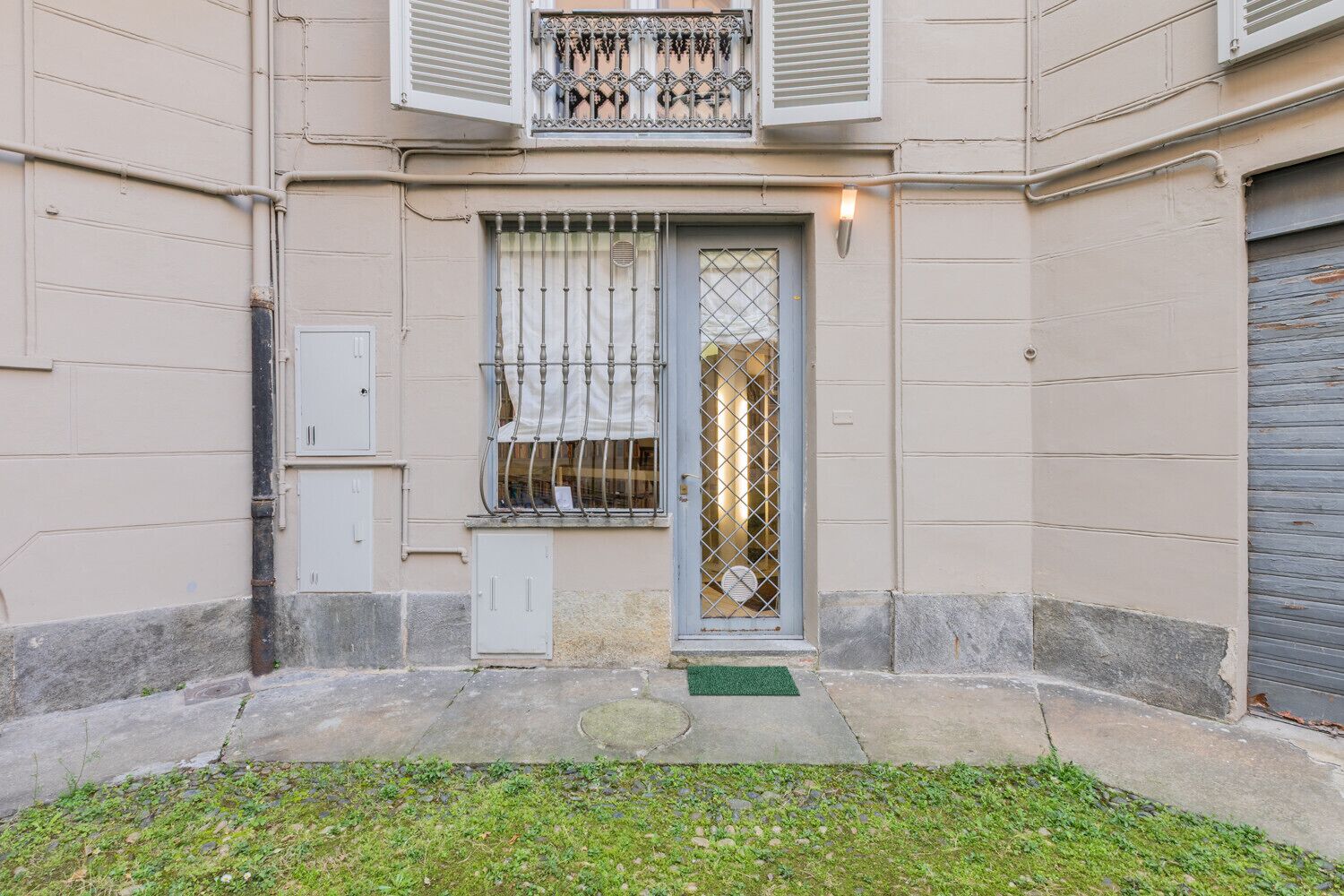 A building with a gated entrance, a small balcony with decorative railings, and a garage door.