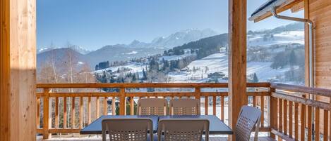 Terraza de madera con mesa y sillas, con vista a un paisaje montañoso nevado.
