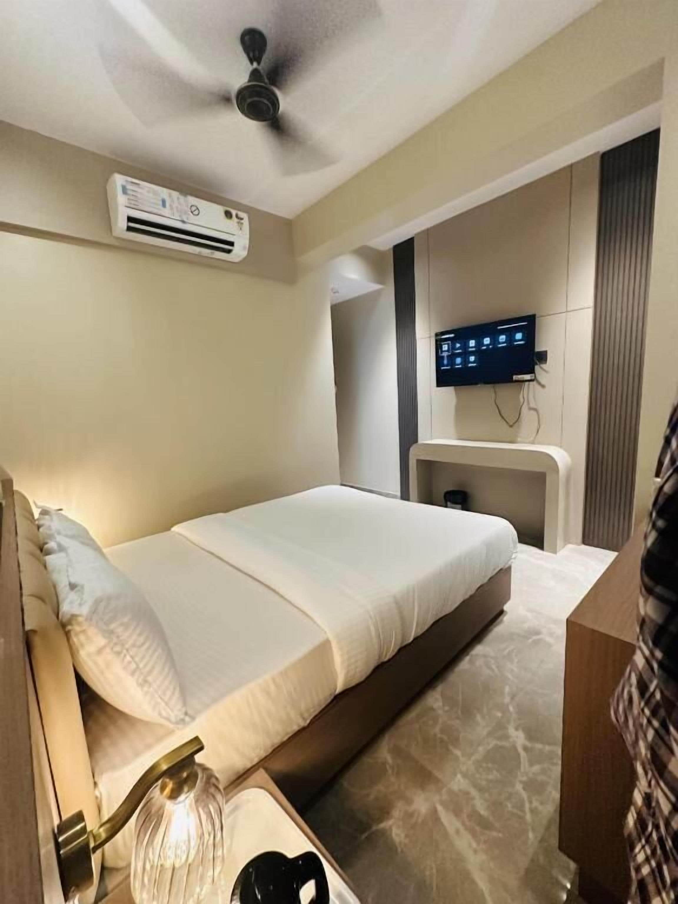A hotel room with a bed, a TV mounted on the wall, and a ceiling fan.