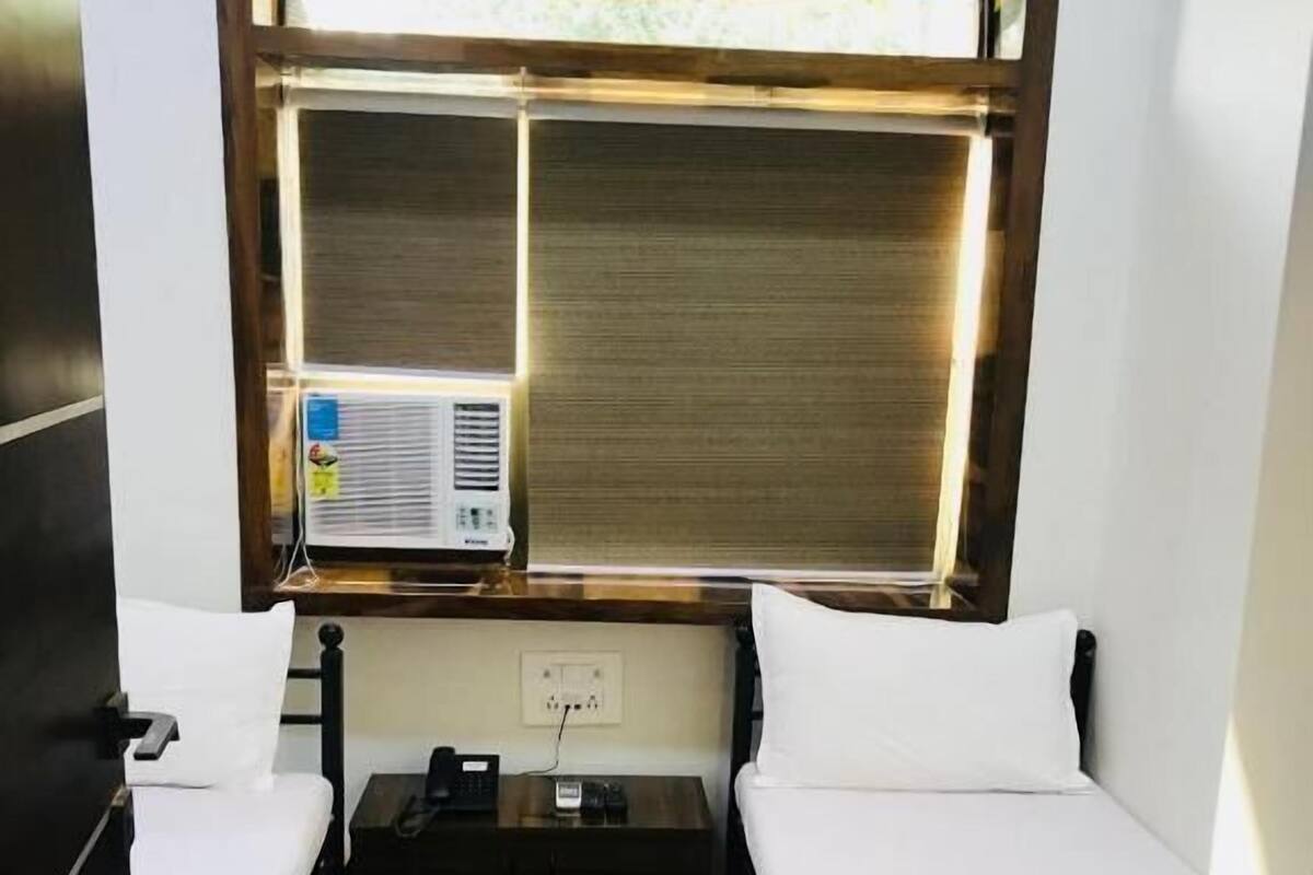 A compact room with two beds, a small table, and a window with blinds.