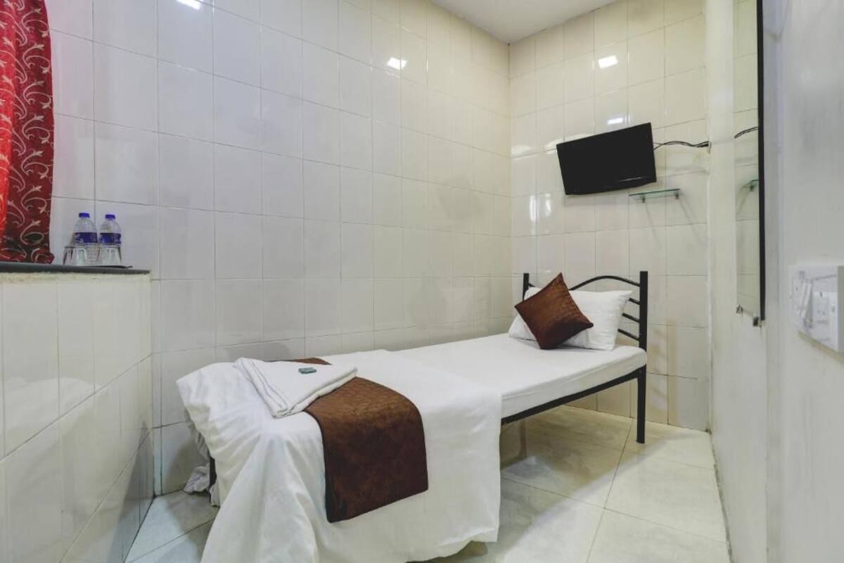 A small, clean room with a single bed, a flat-screen TV mounted on the wall, and a water dispenser on the counter.
