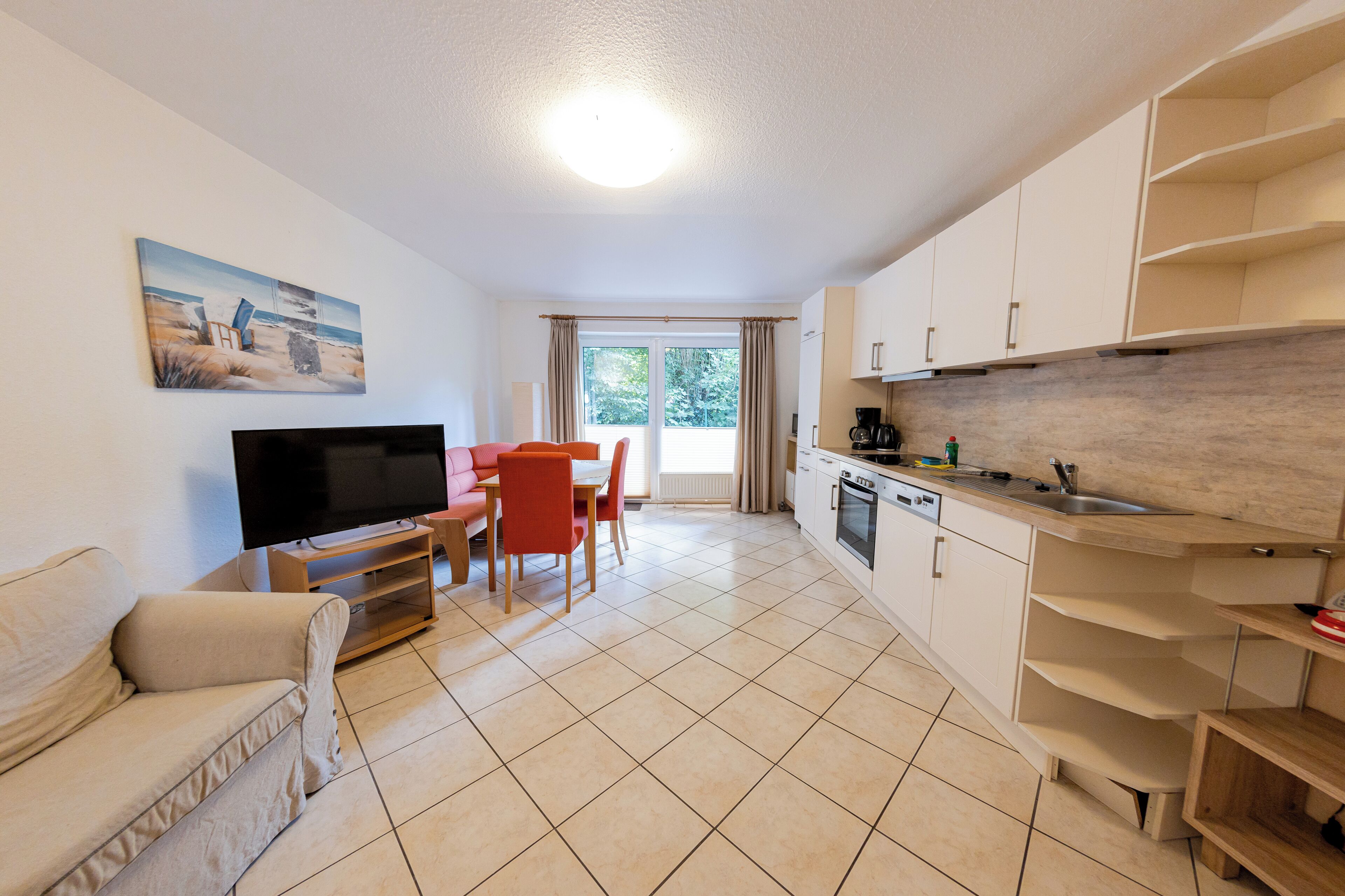 Ein modernes Wohnzimmer mit Sofa, Fernseher und Essbereich. Eine Küche mit Spüle und Schränken ist ebenfalls zu sehen.