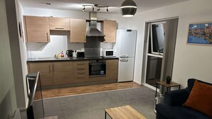 Une cuisine moderne avec des meubles en bois, un four encastré et un réfrigérateur blanc. On y trouve également un coin repas avec une table en bois et un canapé bleu foncé.