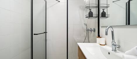 A modern bathroom with a glass-enclosed shower, a white sink with a wooden vanity, and a mirror above the sink.
