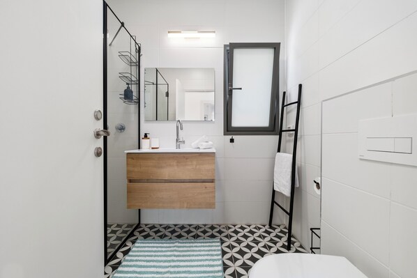 Une petite salle de bain avec un meuble-lavabo en bois, un miroir, un porte-serviettes et un carrelage décoratif.