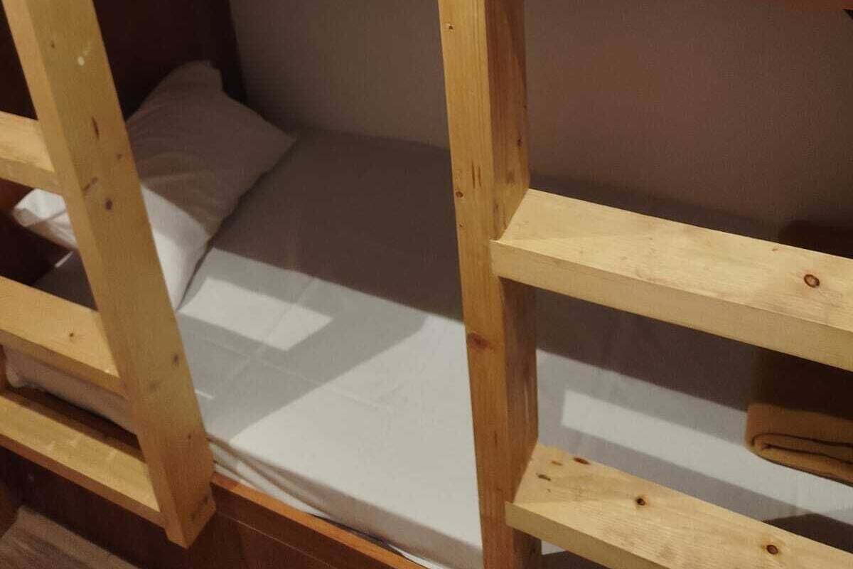 Egy emeletes ágy, fából készült vázszerkezettel, fehér ágyneművel és barna párnával.