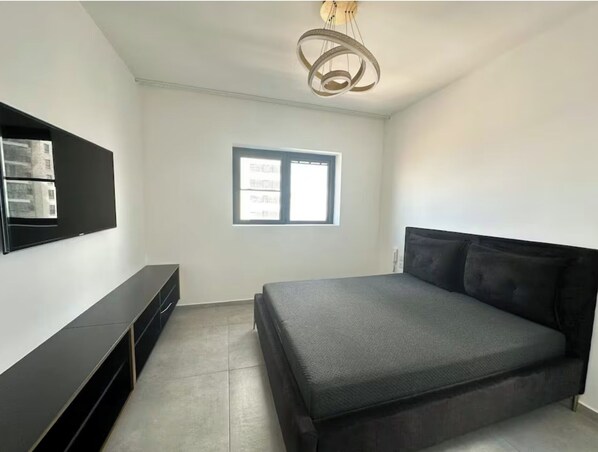 A bedroom with a bed, a TV mounted on the wall, and a window. - Charming 4BR APT with Stellar Sea View (Bat Yam)