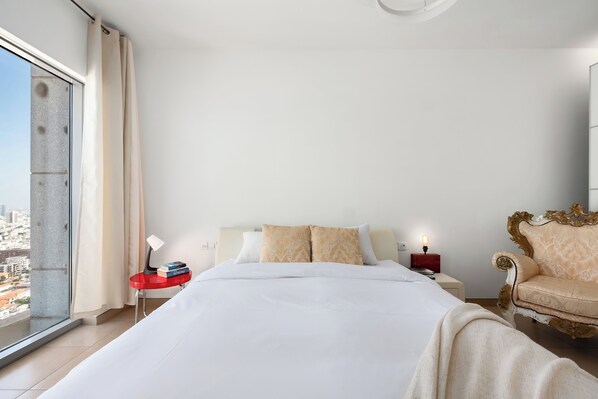Ein modernes Hotelzimmer mit Bett, Nachttisch, Leselampe und Blick auf die Stadt.
