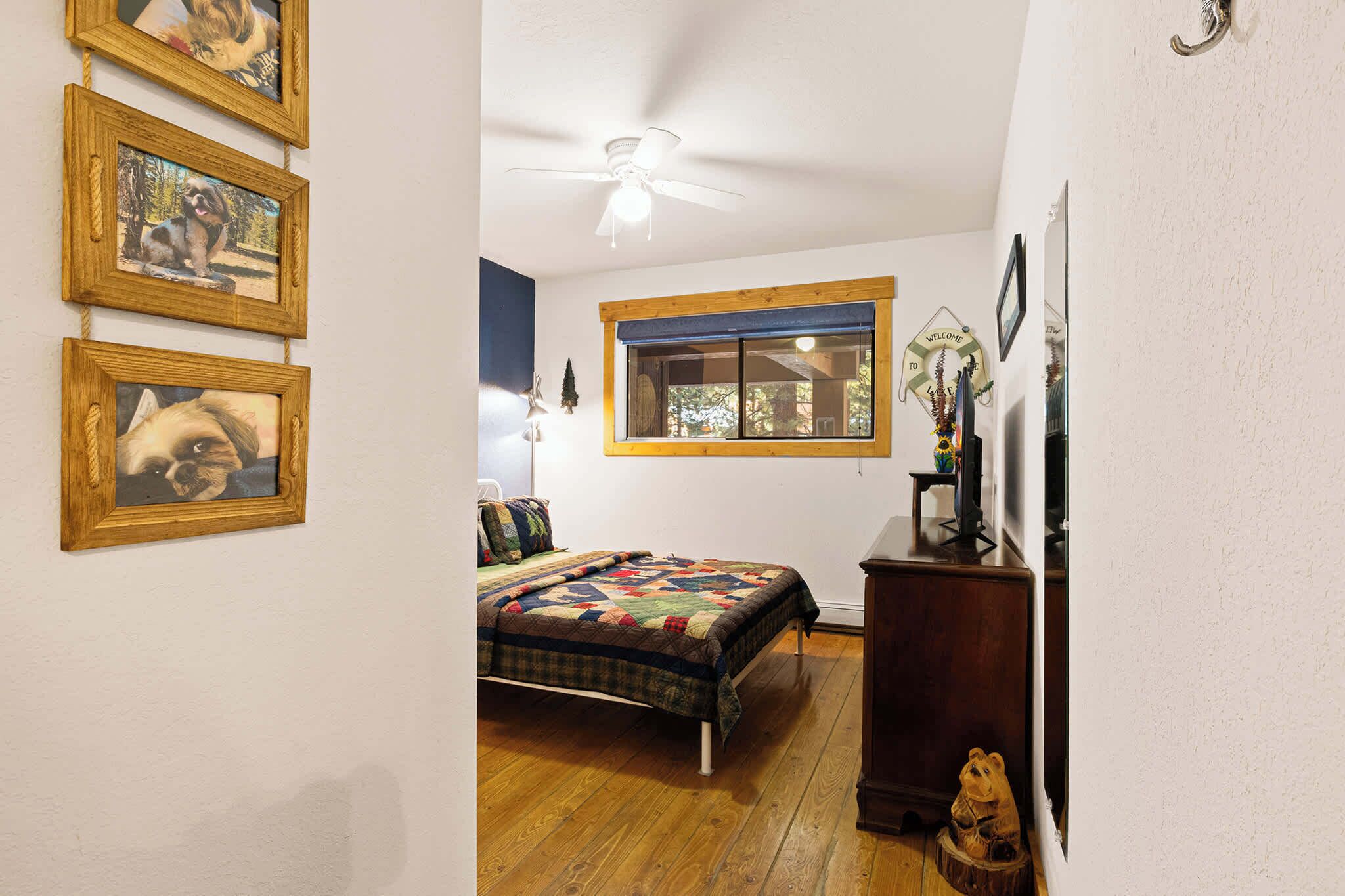 Une chambre à coucher avec un lit, un plancher en bois, un ventilateur de plafond, une fenêtre et des décorations murales.