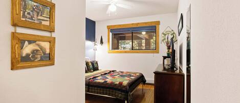 Une chambre à coucher avec un lit, un plancher en bois, un ventilateur de plafond, une fenêtre et des décorations murales.