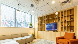 A modern waiting area with a sofa, armchair, and a TV on a wooden shelf. - Student Only Straits Manor (Sheffield)