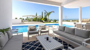Un espacio lounge exterior moderno con piscina, mobiliario blanco y vista al mar.
