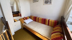 A small, single-bed room with a wooden frame, striped cushions, a white pillow, and two framed pictures on the wall.