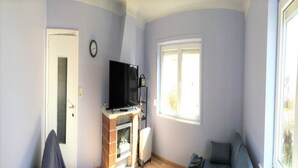 A living room with a sofa, a television on a stand, a window, and a door.