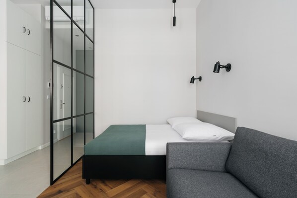 A modern bedroom with a bed, a grey sofa, and a glass partitioned wardrobe. - Native Apartments Długa 24 (Kraków)