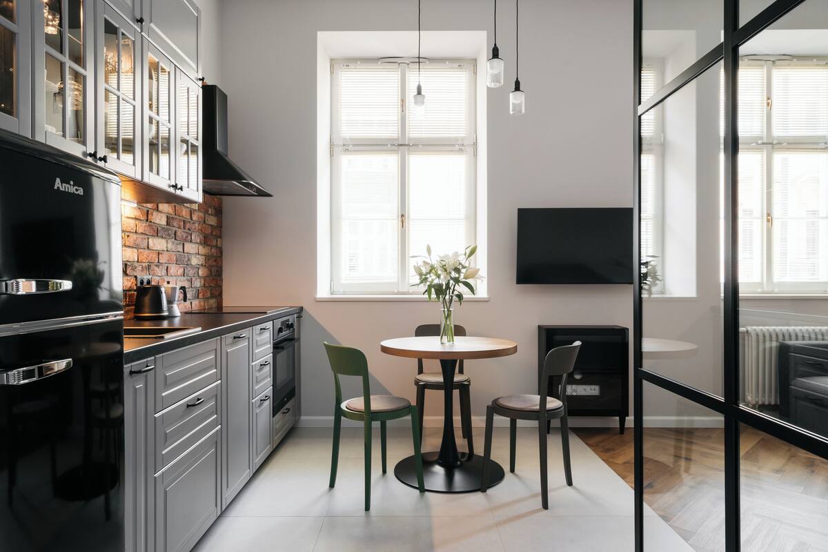Une cuisine moderne avec un mur en briques, des appareils en acier inoxydable et un coin repas comprenant une table ronde et des chaises.