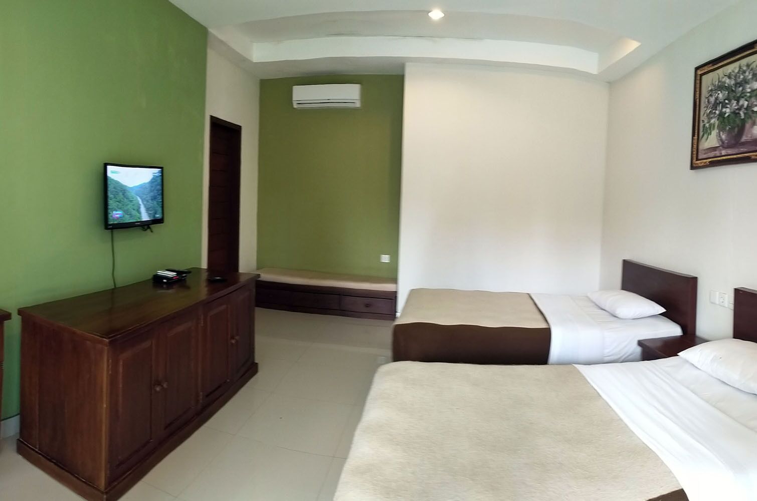 A hotel room with two beds, a wooden dresser, a television, and an air conditioning unit.