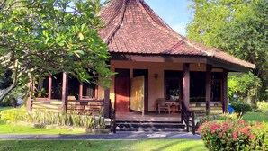 A traditional-style building with a tiled roof, wooden porch, and a small garden area with plants and a bench. - Mascot Beach Hotel Senggigi (Senggigi)