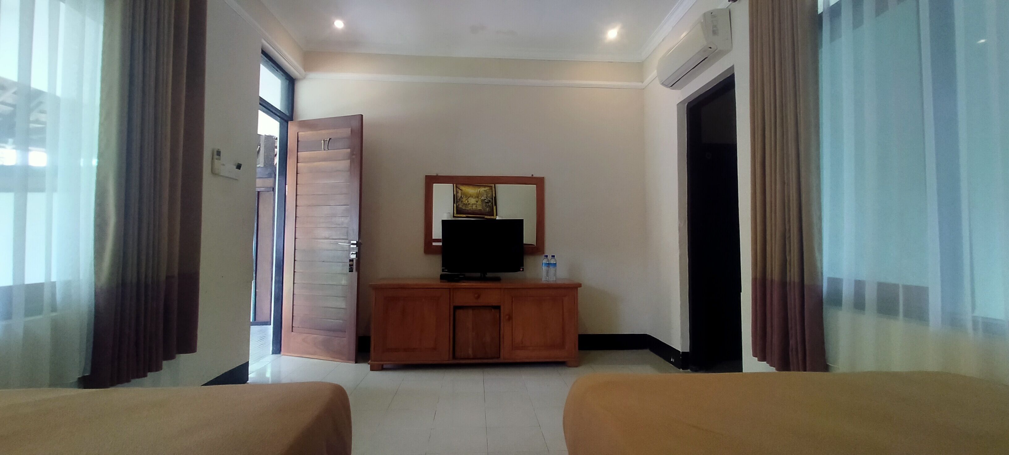 A hotel room with two beds, a wooden cabinet with a television, and a large window with curtains.