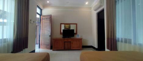 A hotel room with two beds, a wooden cabinet with a television, and a large window with curtains.