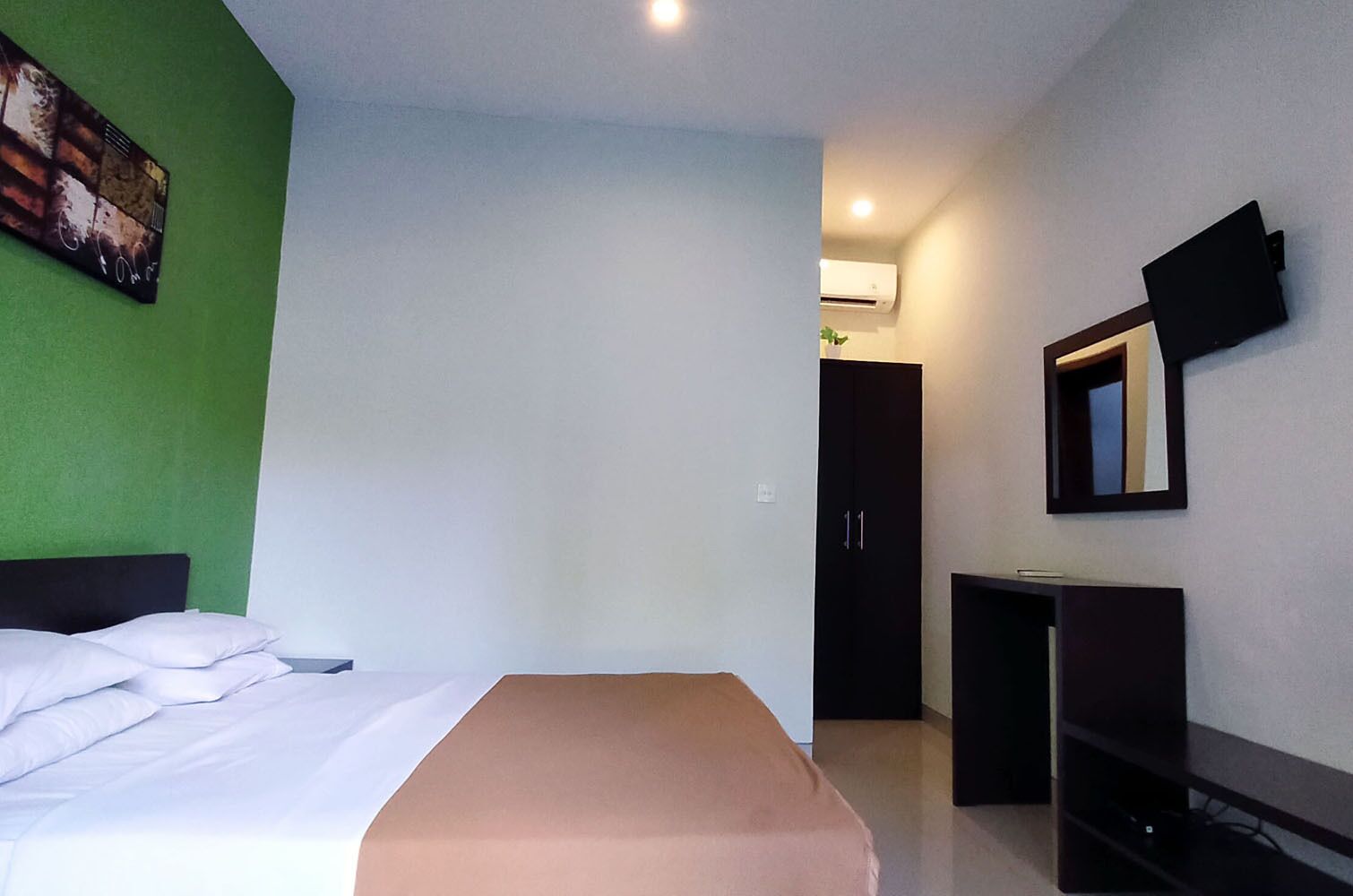 A hotel room with a bed, a desk, a wardrobe, and a mirror.
