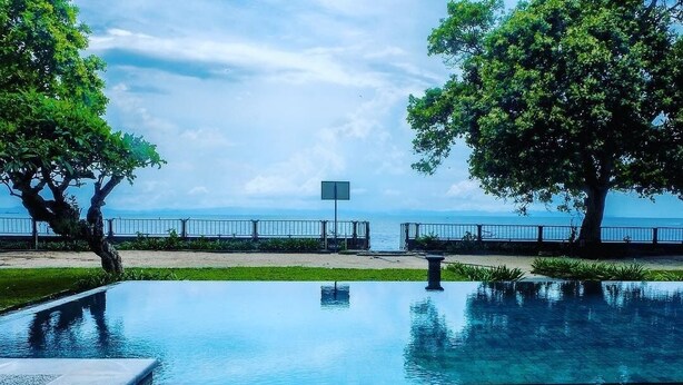A swimming pool with a clear view of the sea, surrounded by trees and a metal fence. - Mascot Beach Hotel Senggigi (Senggigi)