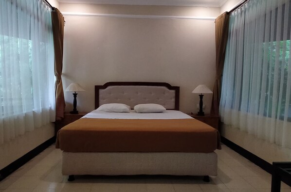 A hotel room with a large bed, two bedside tables with lamps, sheer curtains, and a plain wall. - Mascot Beach Hotel Senggigi (Senggigi)