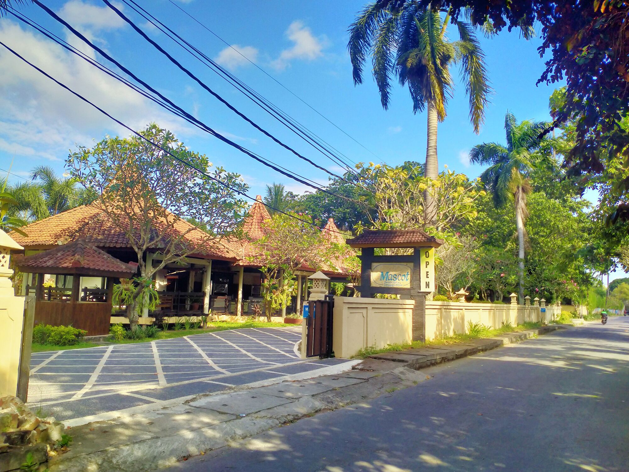 A gated entrance with a sign indicating the property is open, a paved driveway, and a building with a tiled roof.