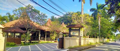 A gated entrance with a sign indicating the property is open, a paved driveway, and a building with a tiled roof.