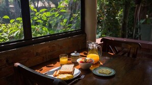 A breakfast table with toast, eggs, fruit, and orange juice, set by a window with a view of greenery. - Sanna Eco Lodge (Arusha)