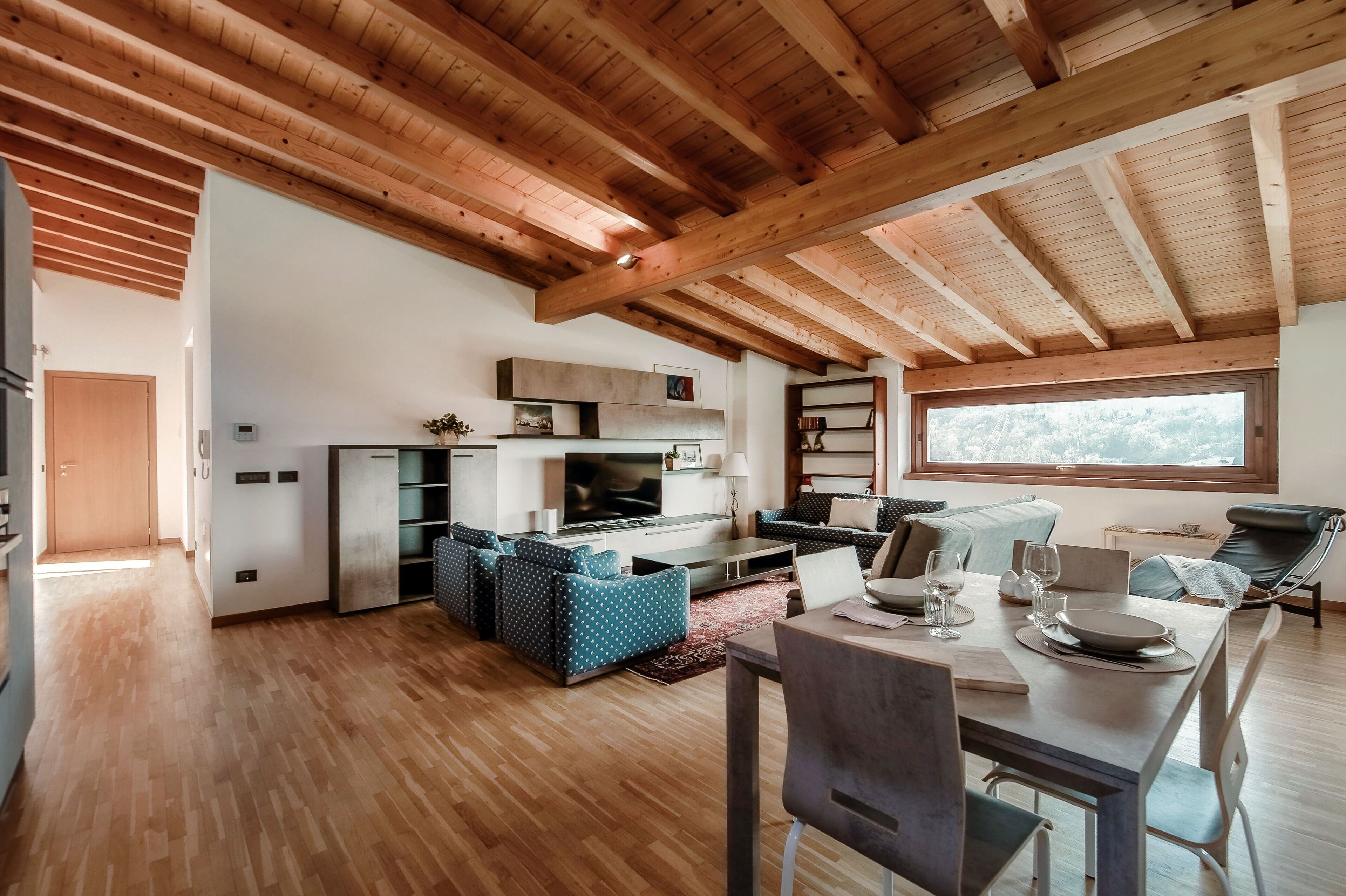 A spacious living area with a wooden ceiling, a dining table set for two, and a kitchen area with modern appliances.