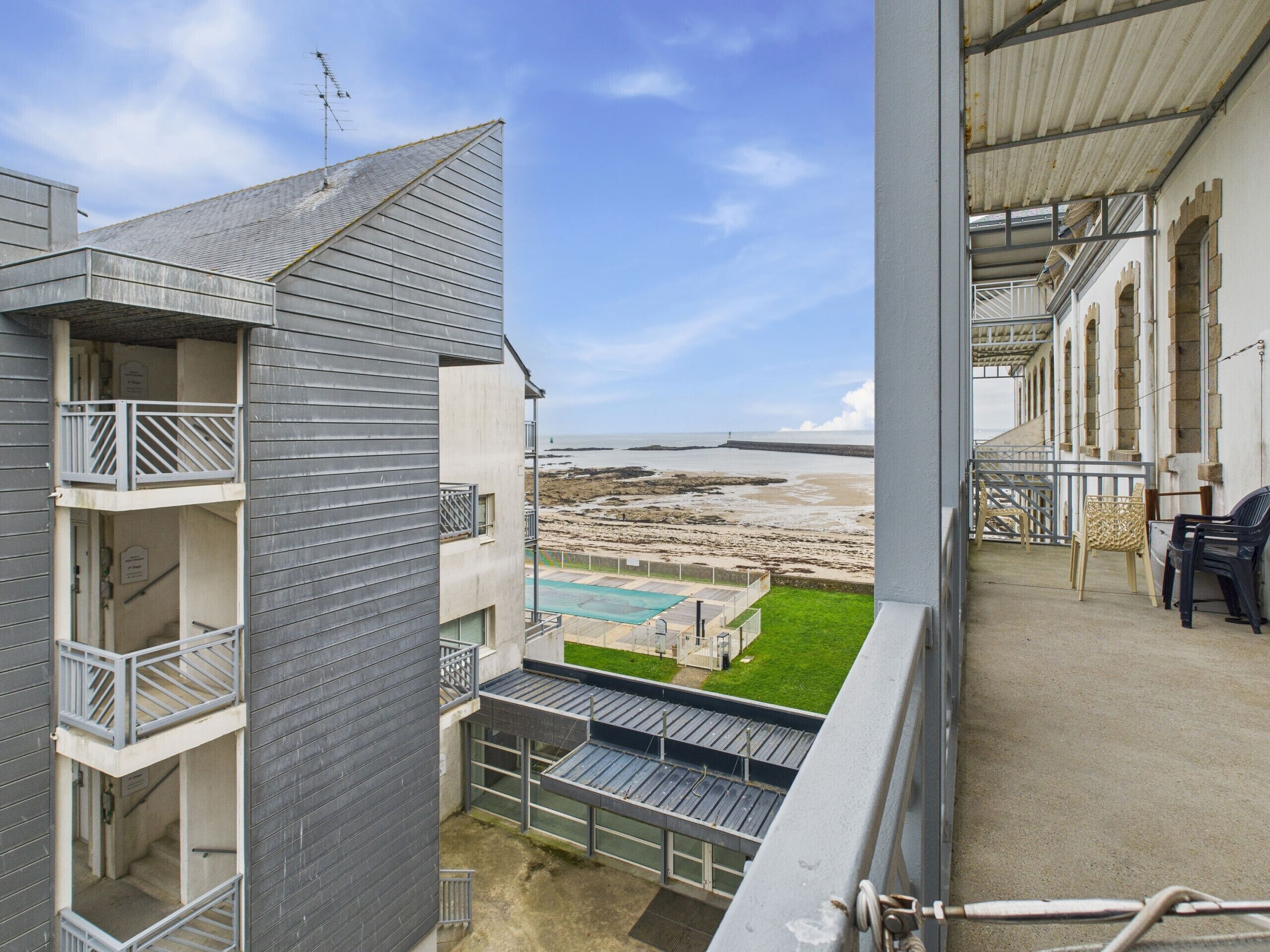 Blick vom Balkon auf Strand, Pool und ein Gebäude mit modernem Design.