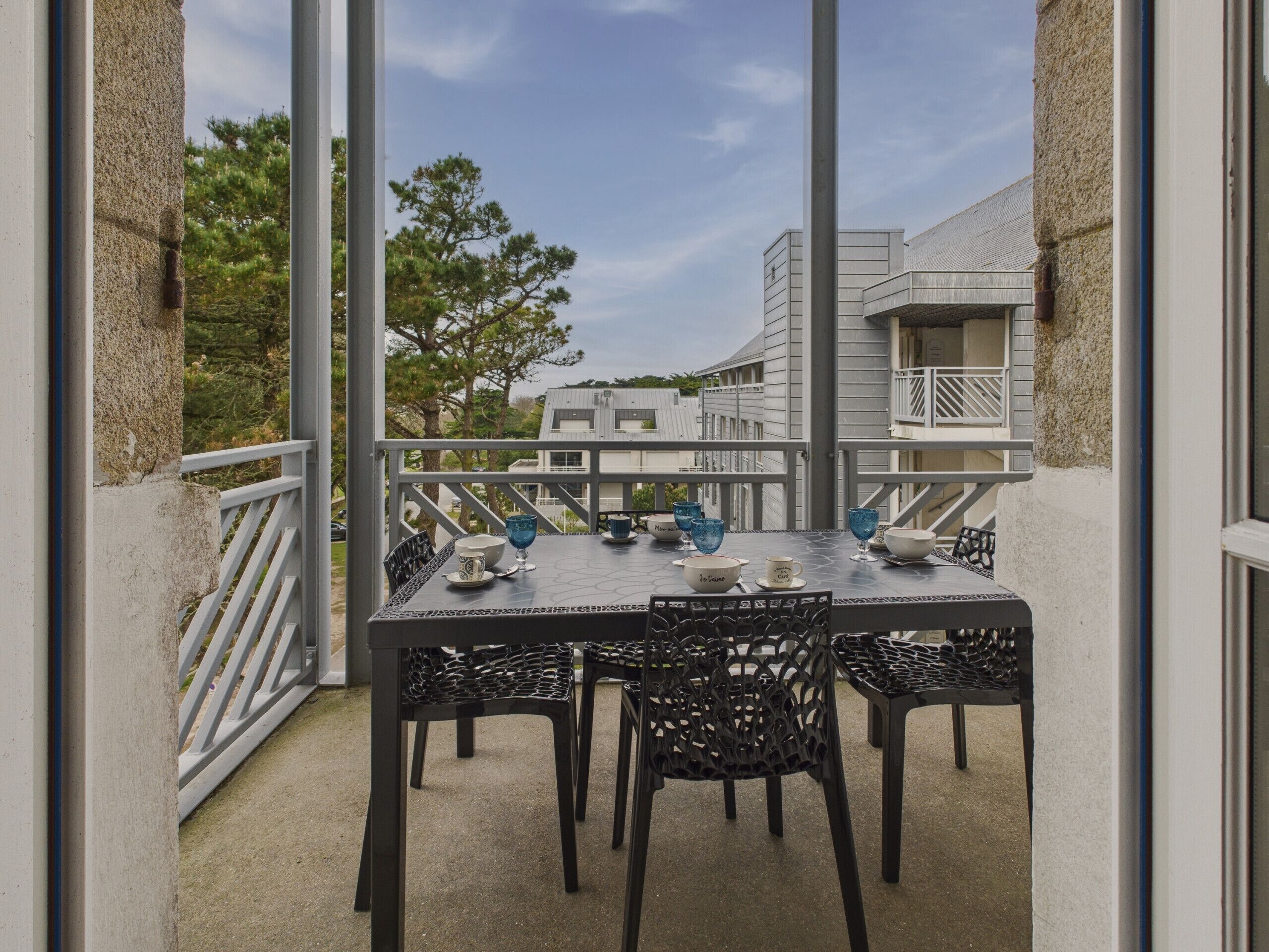 Un balcon avec une table dressée pour les repas, des chaises et une rambarde.
