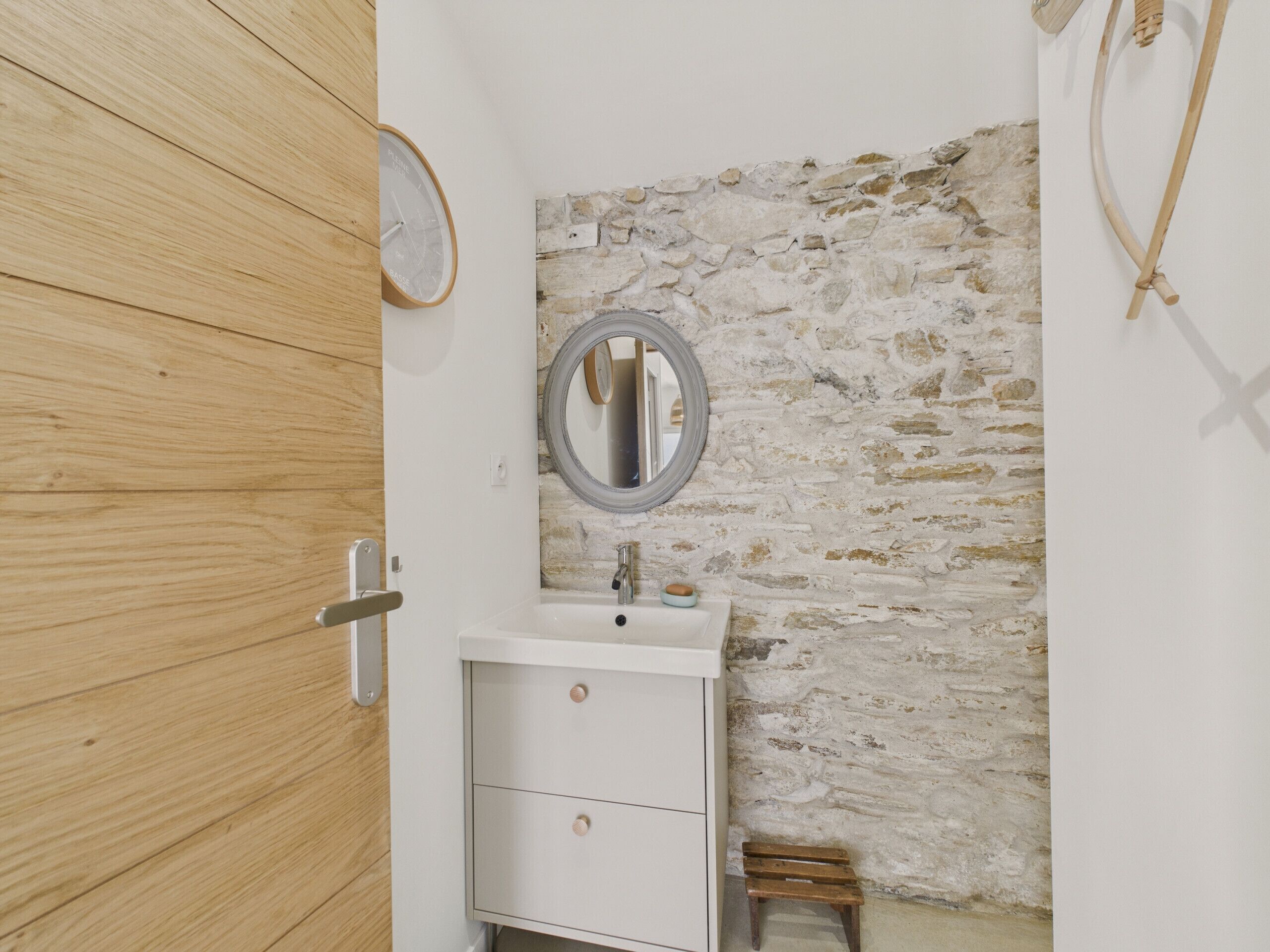Un baño con puerta de madera, un lavabo blanco con espejo y una pared de piedra.