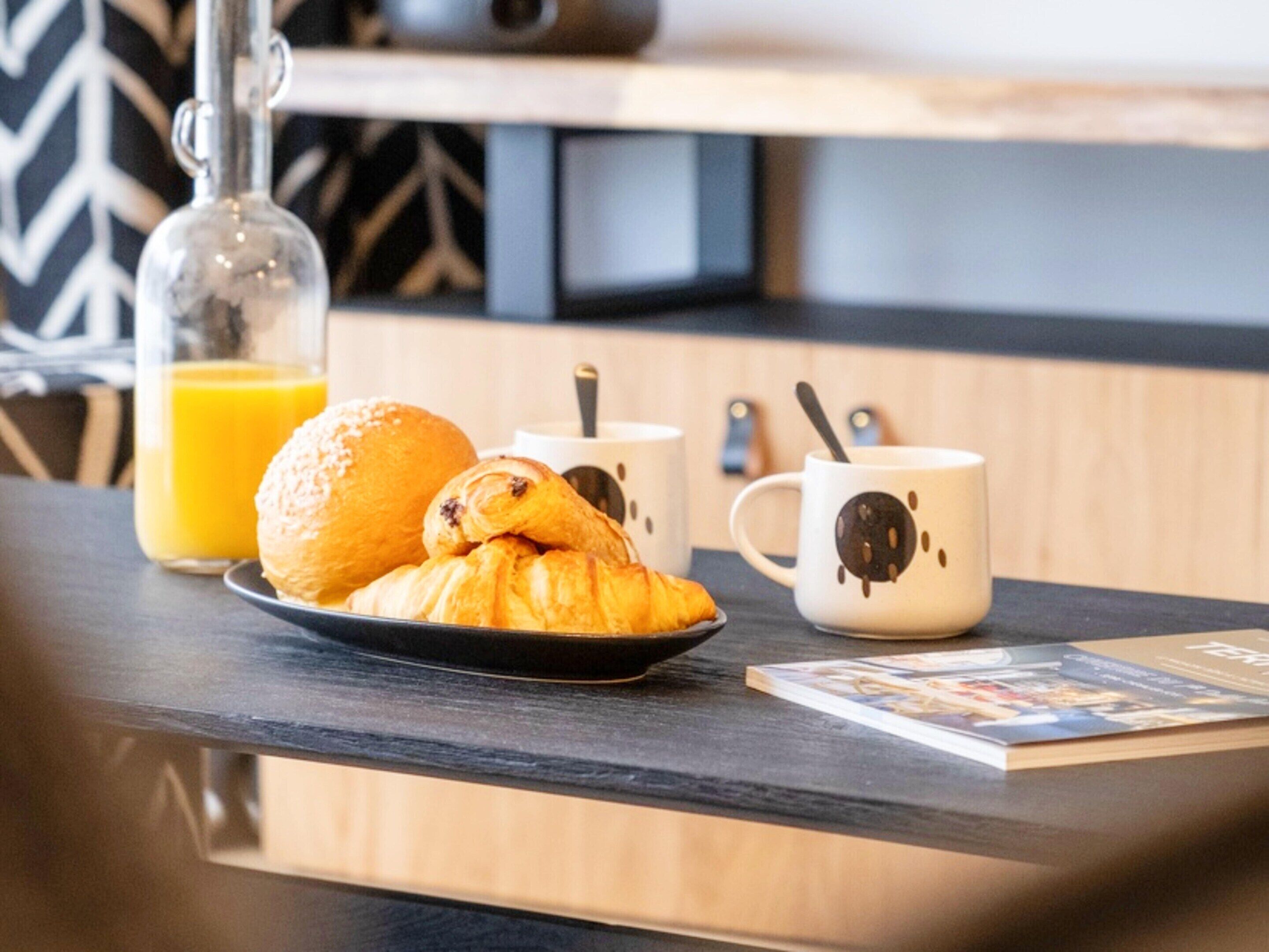 Ein Frühstückstisch mit Croissants, einem Glas Orangensaft und zwei Tassen mit Bärenmotiv.