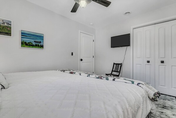 A bedroom with a bed, a ceiling fan, a TV mounted on the wall, and a door. - Bigfoot Manor (Marion)