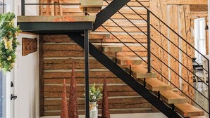 Um interior em vários níveis com escada de madeira, grades de metal e vista para o exterior.