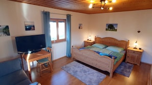 Quarto com cama de madeira, televisão, escrivaninha e uma cadeira.