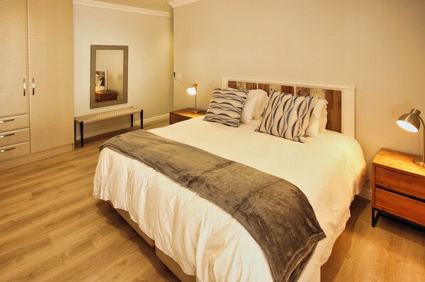 A bedroom with a large bed, wooden floor, a bench, a mirror, and bedside lamps. - Bella Calypso, Langebaan, 8-sleeper (Langebaan)