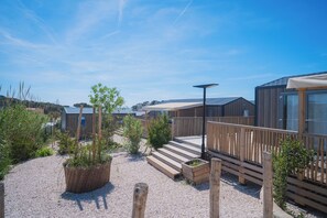Een modern buitenverblijf met houten traptreden die leiden naar een terras, omringd door grind en potplanten.