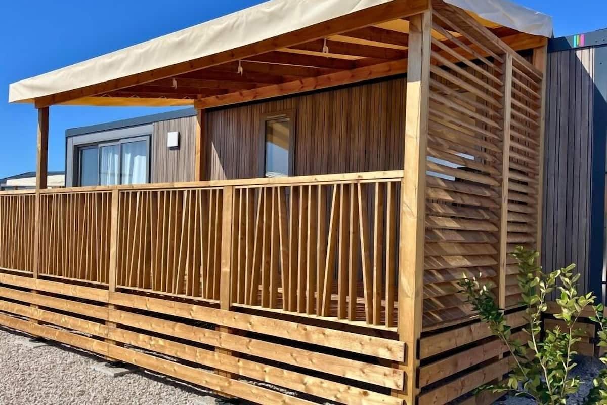 A wooden cabin with a covered balcony, a window, and a door.