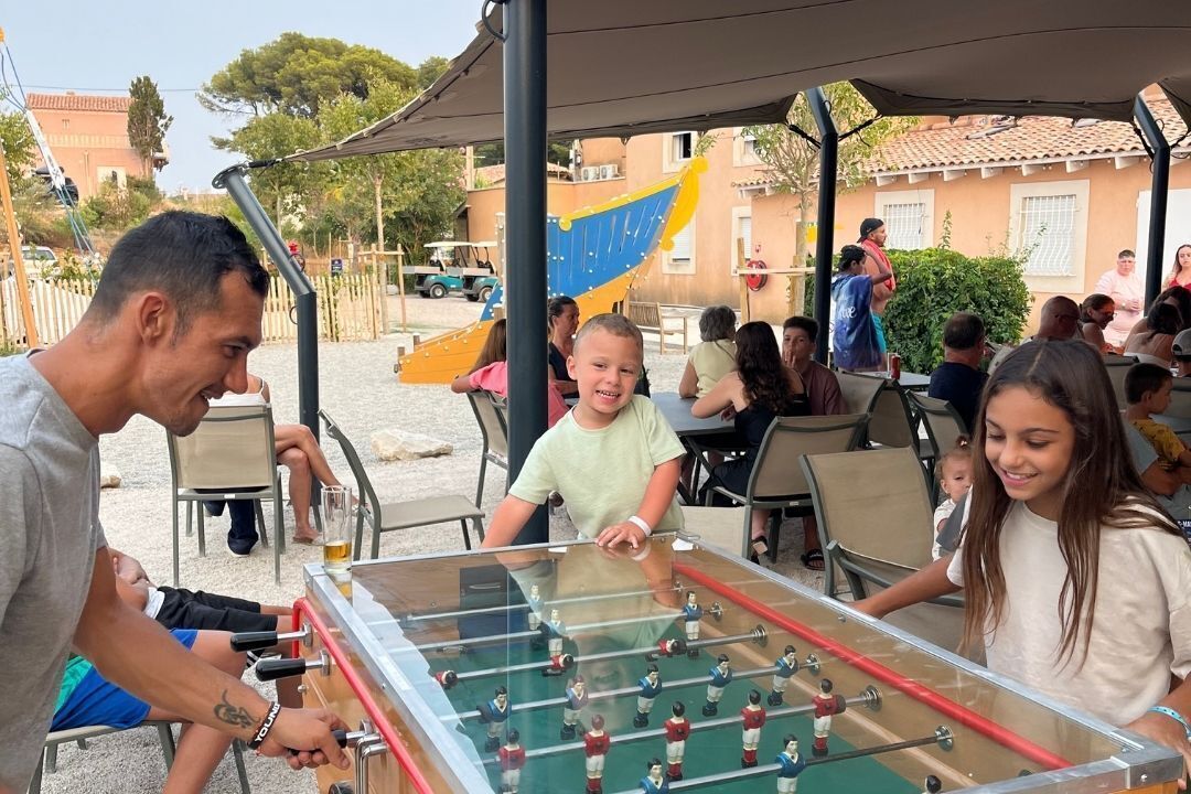 Een tafelvoetbaltafel in een openluchtsetting, met mensen die spelen en toekijken.