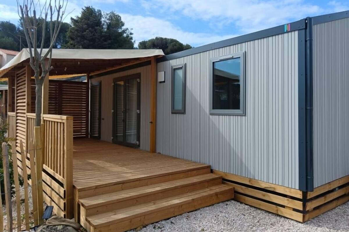 A modern mobile home with a wooden deck and a covered porch.