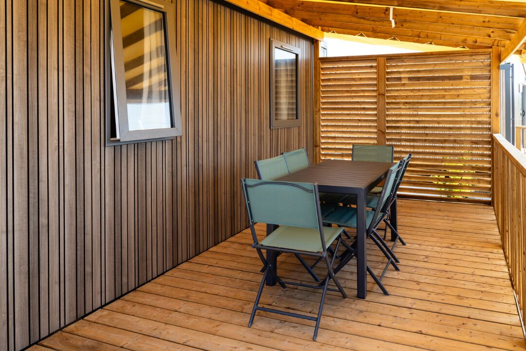 A wooden deck with a table and chairs, enclosed by vertical wooden panels and a slatted wooden fence.