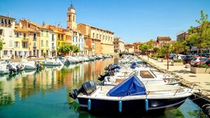 Un canal où sont amarrés des bateaux, un bâtiment historique doté d’une tour, et des immeubles aux couleurs vives qui bordent le quai.