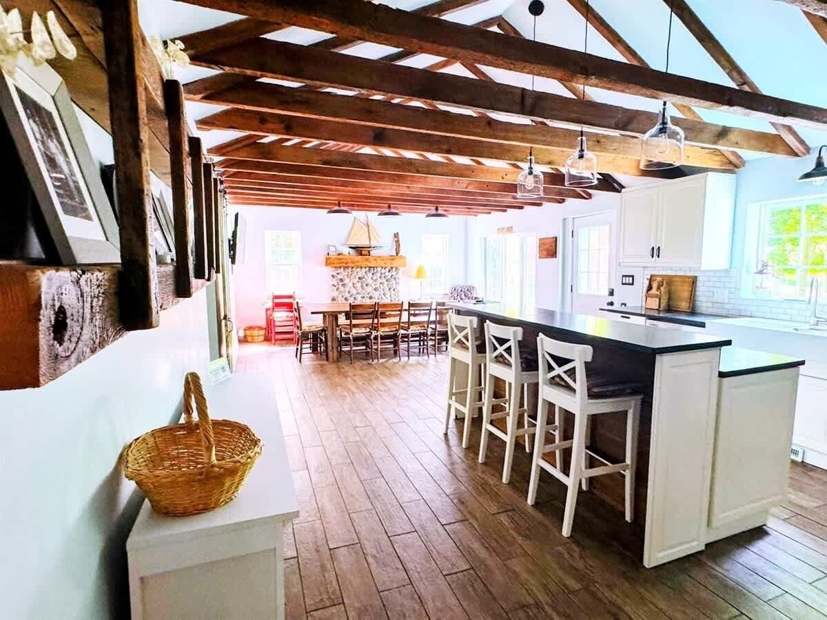 Una cocina con suelo de madera, armarios blancos, una isla central con taburetes de bar y una lámpara colgante.