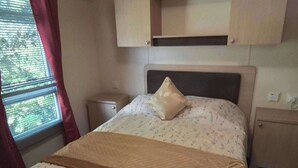 A bedroom with a bed, a nightstand, a small cabinet, and a window with curtains. - Sleep4 Cabin - Self-checkin, Free Parking, Petok (Lowestoft)