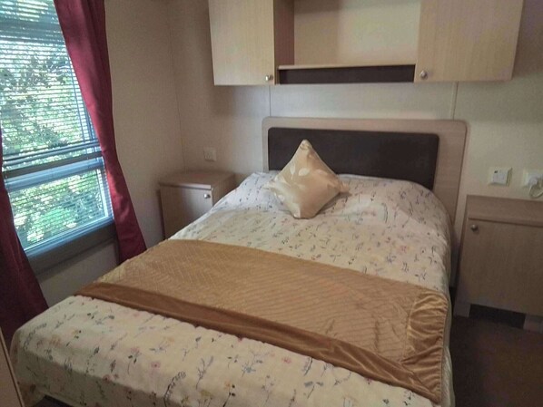 Ein Schlafzimmer mit einem Bett, einem Nachttisch, einer kleinen Kommode und einem Fenster mit Vorhängen.