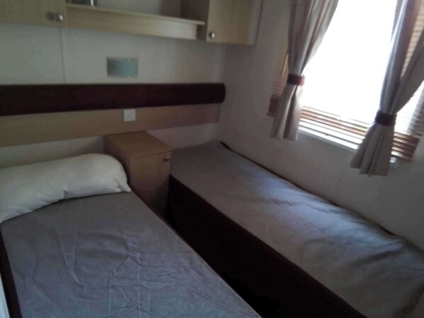 A small, compact room with a single bed, a small cabinet, and a window with curtains. - Sleep4 Cabin - Self-checkin, Free Parking, Petok (Lowestoft)